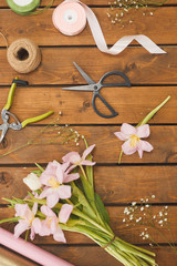 Top view background of pink Spring flowers on wooden table with bouquet decorating supplies, copy space