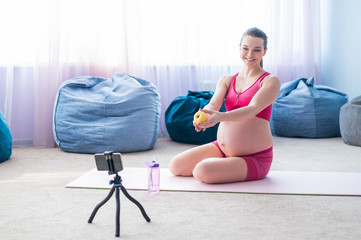 Online lessons for pregnant women. European woman shoots a video fitness lesson on the phone. Waiting for a miracle. Yoga for expectant mothers.