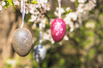 Pink artificial glitter Easter egg hanging on flowering branch of a spring tree. Easter spring holiday concept.