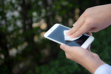 Hands wipe smartphone screen with disinfectant cloth. Close-up cleans  mobile phone standing on outdoor background