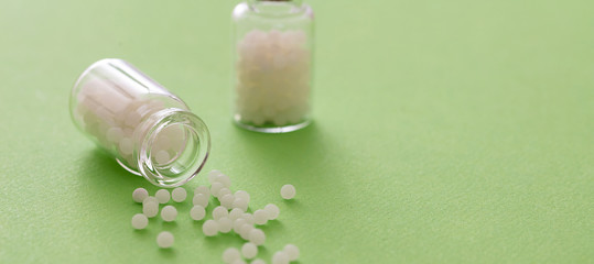 Homeopathy, globules scattered out of glass bottle, green background