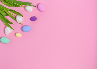 Colored Easter eggs and a bouquet of white tulips on a pink background, copy space, flat lay. Place...