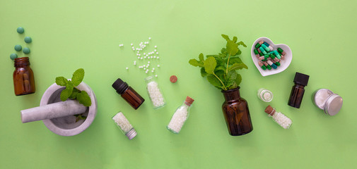 Homeopathy, globules and herbs on green background - obrazy, fototapety, plakaty