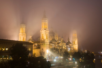 Fototapeta na wymiar Church of our Lady of the Pillar in Zaragoza, Spain, illuminated at night with dense fog and reflections in the river