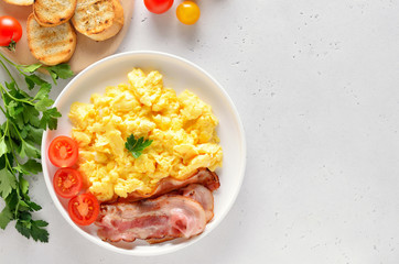 Scrambled eggs, fried bacon and tomatoes on plate