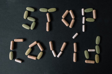 STOP COVID-19 sign written using different color vitamins and drugs. Coronavirus 19. Dark background. Lay flat. Smooth image with shallow depth of field.