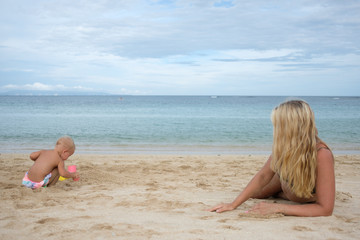 Pregnant mother and daughter sitting on the beach, playing with sand on summer vacations.