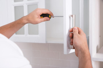 Fototapeta Worker installing handle of cabinet door with screwdriver in kitchen, closeup obraz