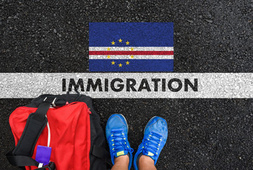 Man in shoes with bag standing next to line with word IMMIGRATION and flag of Cape Verde on asphalt road