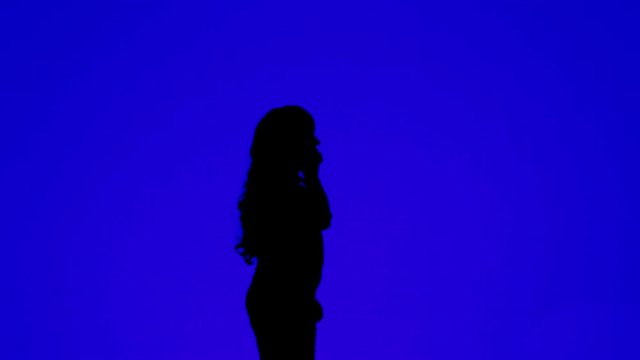 Silhouette of a woman with curly hair talking on a cell phone on a blue background