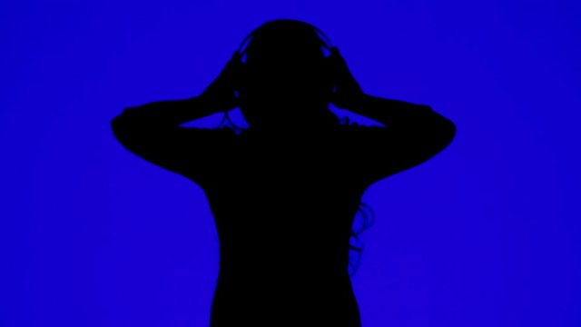 Silhouette of a woman wearing headphones and dancing to the music on a blue background