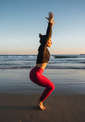 Fototapeta na wymiar Woman practicing a variation of the Utkatasana yoga position on the beach