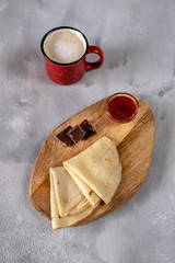 Crepes with raspberry jam and chocolate on a wooden board top view. Golden pancakes with a coffee...