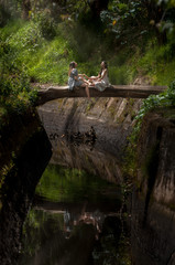 Fototapeta na wymiar mother and daughter sitting face to face on a rustic wooden bridge bathed in the sun on a river in the middle of nature