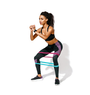 Sporty woman doing squats with resistance band. Photo of african american girl in black sportswear on white background. Strength and motivation