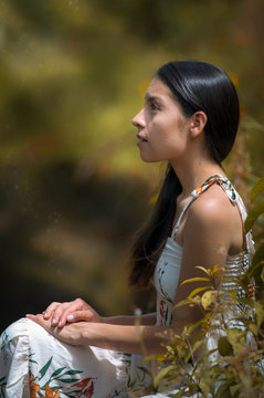 Young Woman With Dress Sitting In The Middle Of Nature With Her Hands Crossed On Her Knees