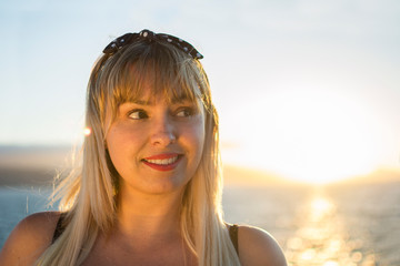Portrait of a blonde woman with the sunset sun behind her, reflecting in the sea.