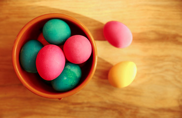 Colored eggs in a brown bowl on a wooden background