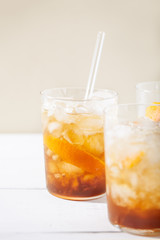 Cold brew coffee mocktail with orange peel and glass straw close-up.Glass with citrus esprecco tonic with ice on white background.Refreshing summer non-alcoholic drink concept.Vertical orientation