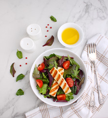 Green salad with fried halloumi cheese in a white plate on a marble background, top view. 