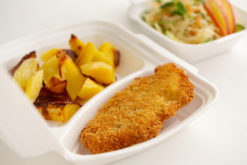 food delivery in white lunch boxes. Food to go. Fried potatoes and chicken chop. Cabbage salad. 