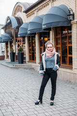 young woman in a scarf poses on the streets of the city at a cafe