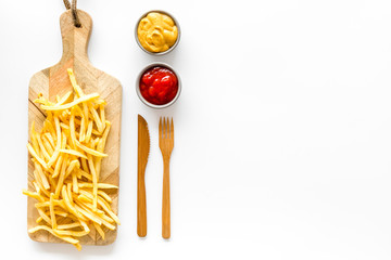 Fast food restaurant concept. French fries on cutting board near sauces on white table top-down copy space