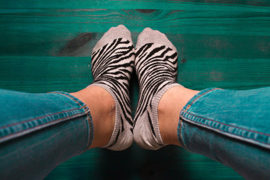 Imagen de unos pies adolescentes con calcetines de cebra animal print y vaqueros azules de estilo vintage con fondo verde