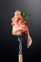 Thin sliced prosciutto with parsley on a fork. Traditional Italian cuisine.