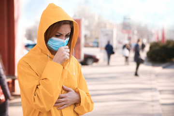 Obraz premium Woman with medical mask coughing on city street. Virus protection