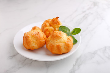 Profiteroles with custard decorated with mint on a marble background