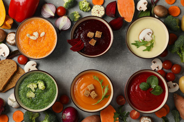Vegetable soups and ingredients on grey background, top view
