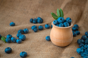 Fresh organic blueberries in a wooden bowl on a sackcloth background. Juicy and fresh blueberries with green leaves on rustic table. Bilberry on wooden Background. Blueberry antioxidant