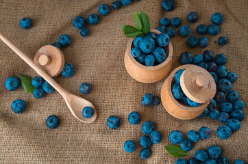 Fototapeta na wymiar Fresh organic blueberries in a wooden bowl on a sackcloth background. Juicy and fresh blueberries with green leaves on rustic table. Bilberry on wooden Background. Blueberry antioxidant