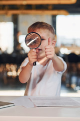 Smart child in casual clothes with laptop on table have fun with magnifying glass