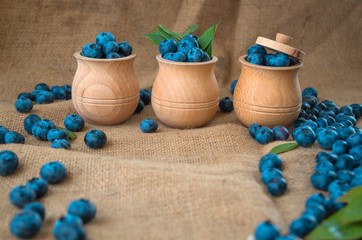 Fresh organic blueberries in a wooden bowl on a sackcloth background. Juicy and fresh blueberries with green leaves on rustic table. Bilberry on wooden Background. Blueberry antioxidant
