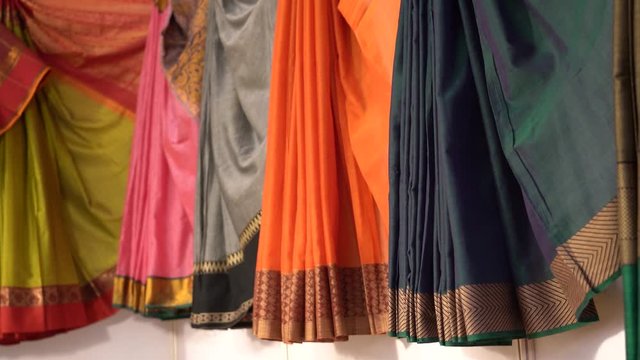 Multicolored festive Indian sarees, pleated and hung for display in a shop. Simple and elegant women wear