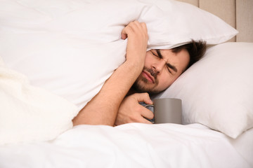 Sick young man with cup of hot drink in bed at home. Influenza virus