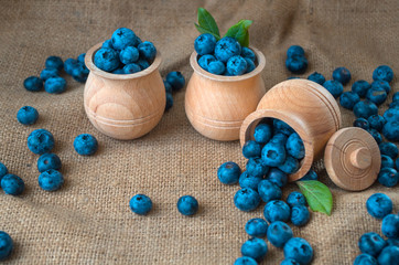 Fresh organic blueberries in a wooden bowl on a sackcloth background. Juicy and fresh blueberries with green leaves on rustic table. Bilberry on wooden Background. Blueberry antioxidant