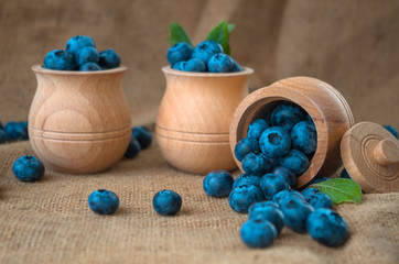 Fresh organic blueberries in a wooden bowl on a sackcloth background. Juicy and fresh blueberries with green leaves on rustic table. Bilberry on wooden Background. Blueberry antioxidant