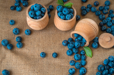 Fresh organic blueberries in a wooden bowl on a sackcloth background. Juicy and fresh blueberries with green leaves on rustic table. Bilberry on wooden Background. Blueberry antioxidant