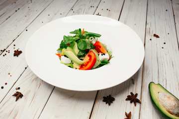Bright vegetable salad on a white plate. Salad of tomatoes, herbs, cheese and avocado. The table is decorated with avocado and star anise.