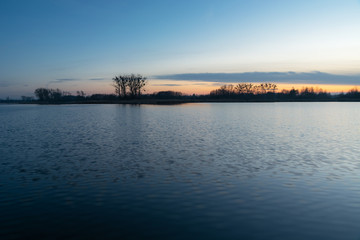 Calm water, trees on the horizon and the sky after sunset