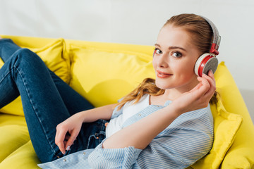 Side view of smiling girl in headphones looking at camera on couch