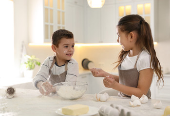 Cute little children cooking dough together in kitchen