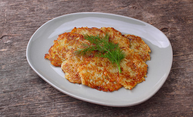 Potato pancakes in a plate decorated with dill on a rustic background
