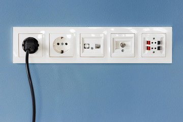 Black cable plugged in a white electric outlet, blue background