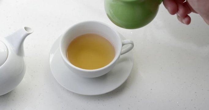Pouring milk into black ceylon tea teapot cup 