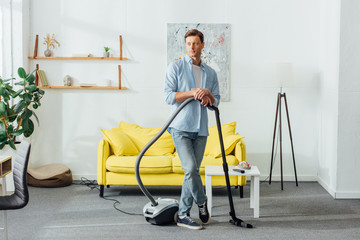 Fototapeta na wymiar Handsome man looking away while holding vacuum cleaner in living room