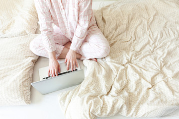 Mobile Office at home. Young woman in pajamas sitting on bed at home working using on laptop pc...
